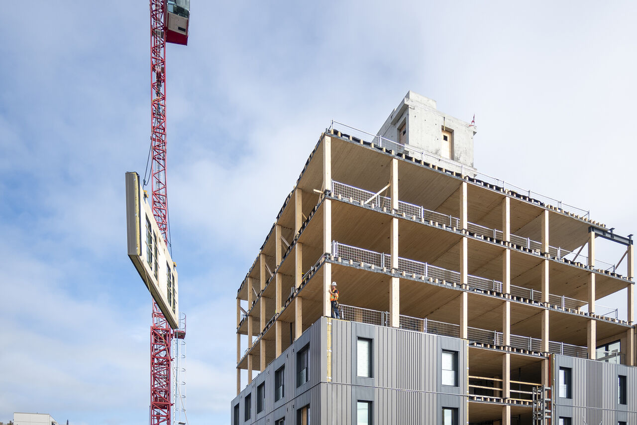 Tower crane lowering a prefabricated panel toward the mass timber structure